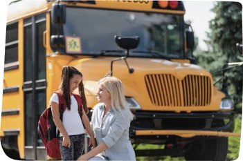 A child boarding a yellow nursery bus under the supervision of a female bus attendant, emphasizing the safety measures provided by Step by Step Nursery.