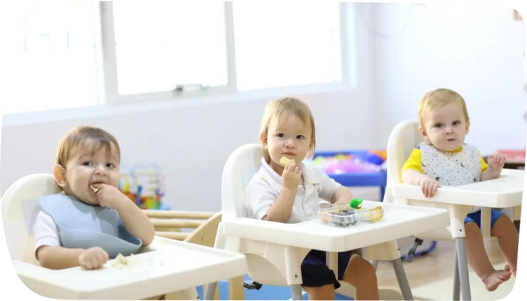 Babies seated in high chairs enjoying mealtime at Step By Step Nursery Dubai, promoting social interaction and sharing skills.