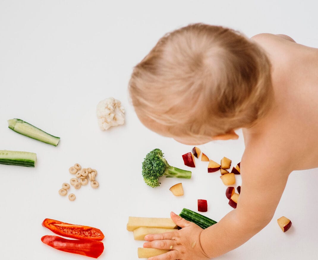 A toddler exploring vegetables like broccoli, cucumber, and red peppers during a sensory learning activity, with Step By Step Nursery Dubai promoting healthy eating habits through interactive experiences.