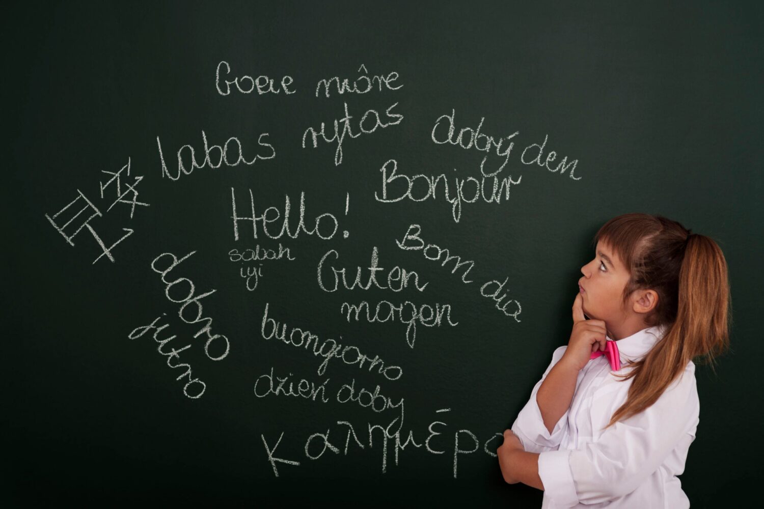 Small girl standing in front of blackboard with multiple phrases in foreign languages